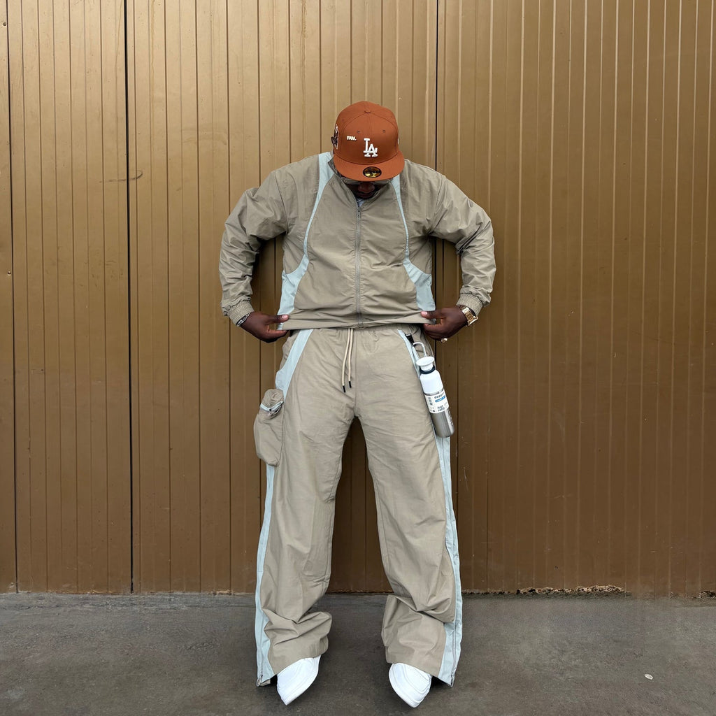 Person wearing a beige jumpsuit with white accents and a brown cap against a brown wall.