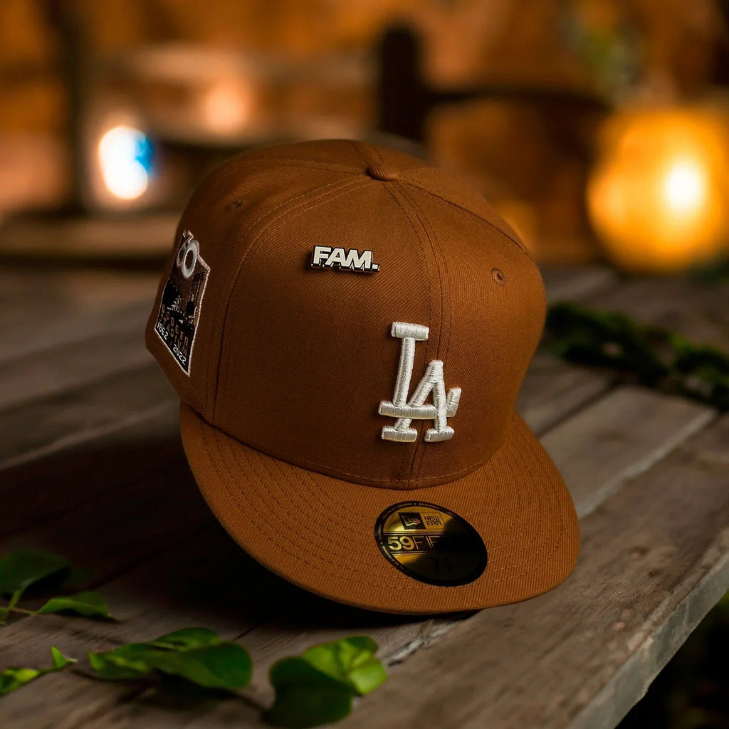 Brown cap with 'FAM' and 'LA' logo on a wooden surface with blurred lights in the background