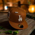 Brown cap with 'FAM' and 'LA' logo on a wooden surface with blurred lights in the background
